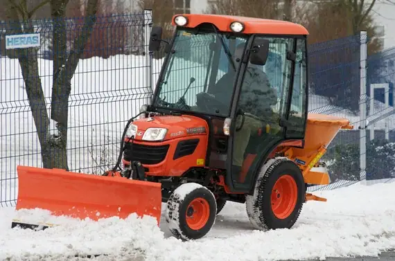 Kommunaltraktor mit Schneepflug räumt einen verschneiten Weg